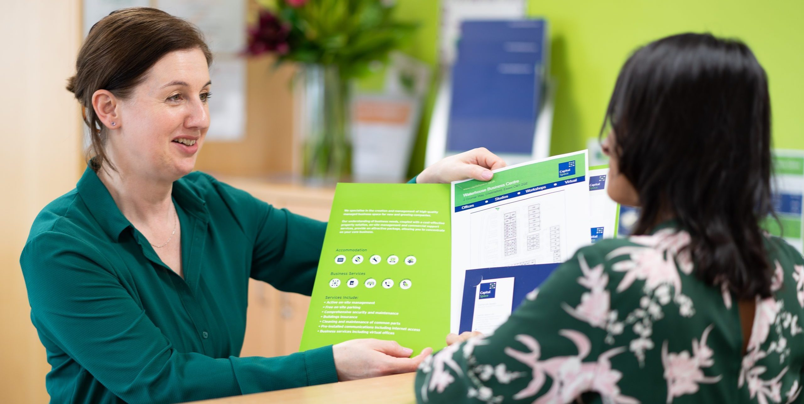 Receptionist shows information folder to visitor